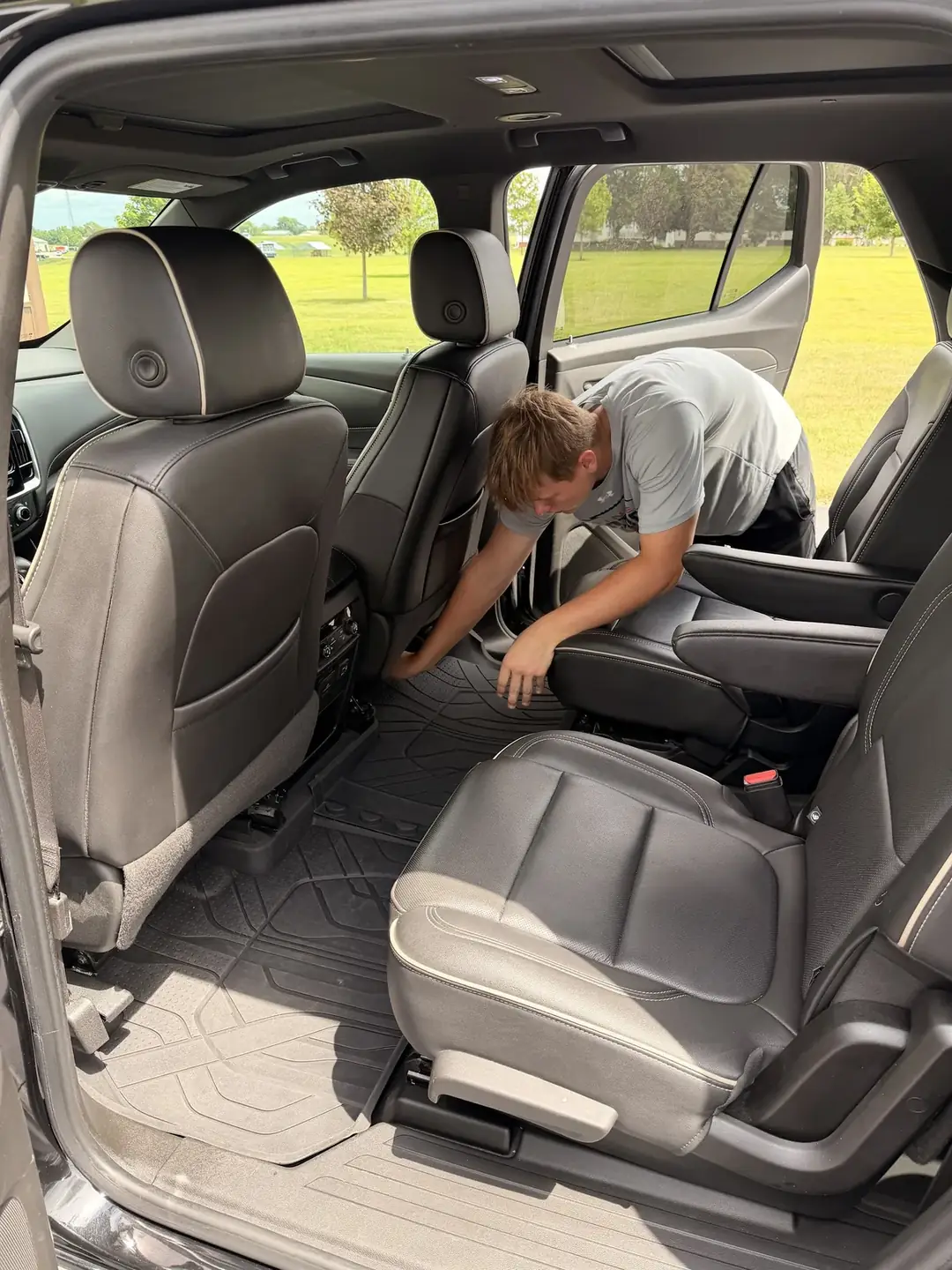 A detailer cleaning the floor behind the front seats of an SUV