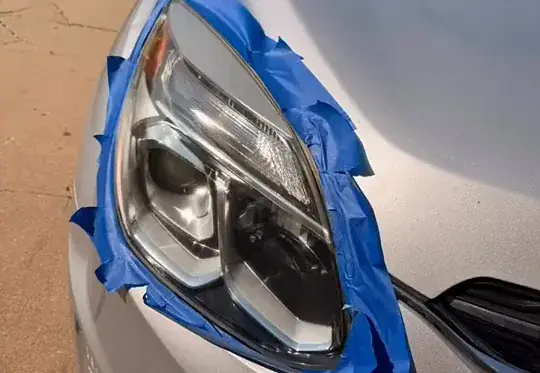The same headlight polished clear again, with masking tape still on the trim