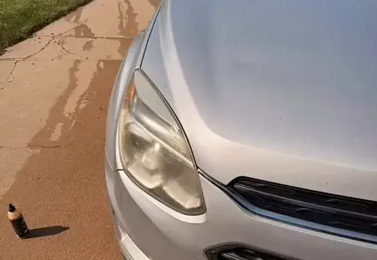 A yellowed, cloudy headlight on a silver Chevrolet before restoration